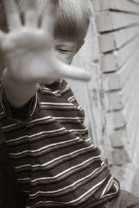 Boy with eyes closed, reaching towards viewer with open palm as a defensive measure.