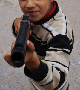 Smiling boy holding toy gun towards viewer.
