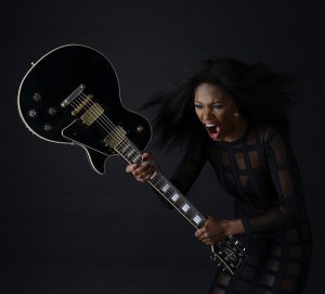 Angry woman, shouting, apparently about to smash an electric guitar.